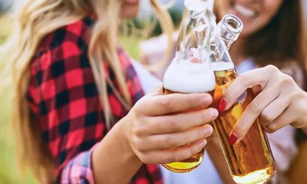 Un groupe de jeunes femmes trinque avec des bouteilles de bière.